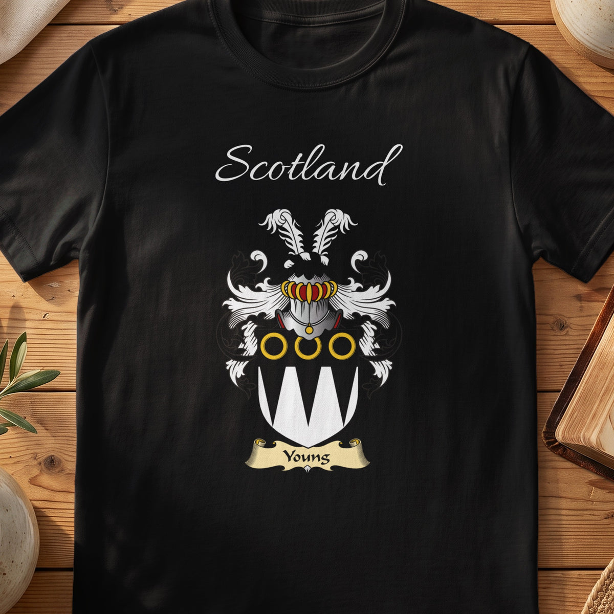 Black Youngs Scottish family crest T-shirt laid flat, showing “Scotland” above a black-and-silver shield with pale pointed panels and gold rings.