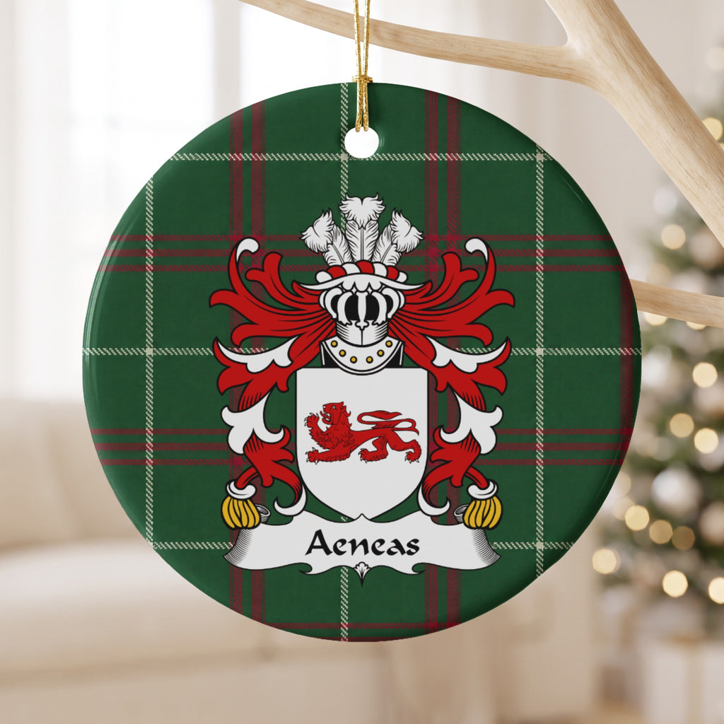 Aeneas family crest and surname on a round Welsh national tartan ornament, hanging by a gold cord from a pale wooden branch with blurred Christmas lights behind it.