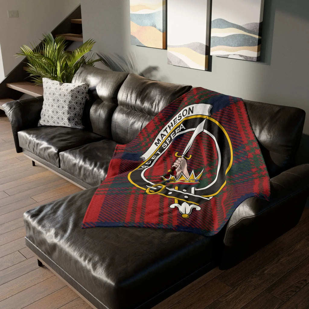 Clan Matheson crest tartan throw blanket draped over leather sofa — red tartan with clan crest, 50x60 inch polyester
