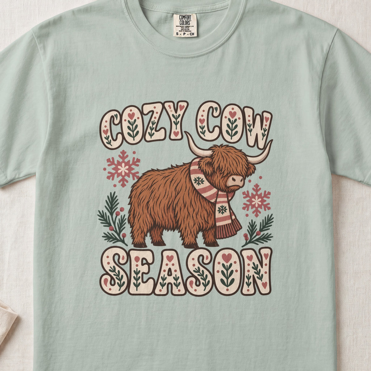 Cozy Cow Season Highland cow design on a Bay Comfort Colors 1717 T-shirt, flat lay