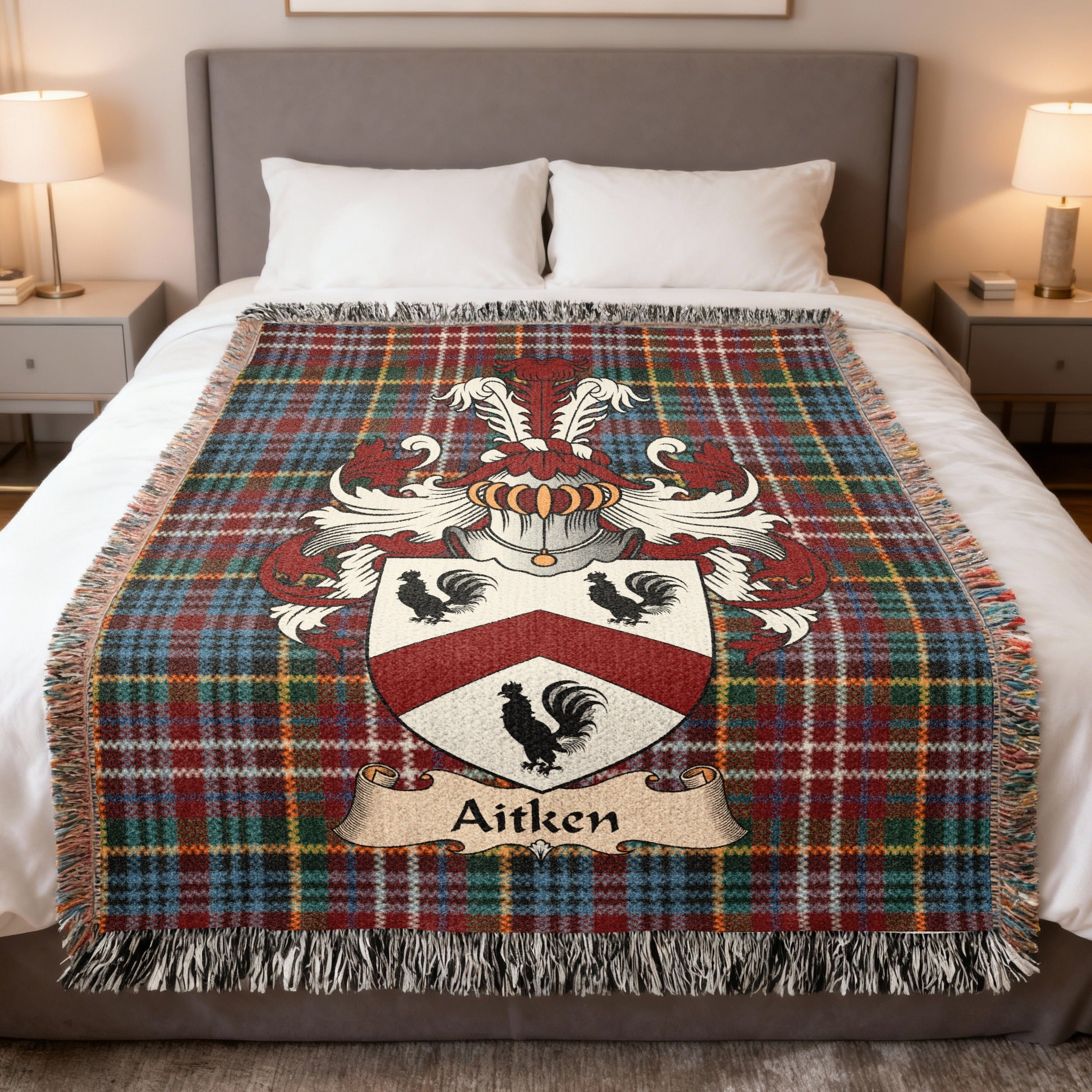 Aitken Scottish family crest woven blanket on a Caledonia tartan background, displayed on a bed