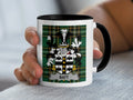 White mug with black rim and handle, featuring a green plaid pattern and a coat of arms with the name BATT.