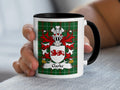 White mug with black handle featuring the Clarke family crest on a green tartan background.