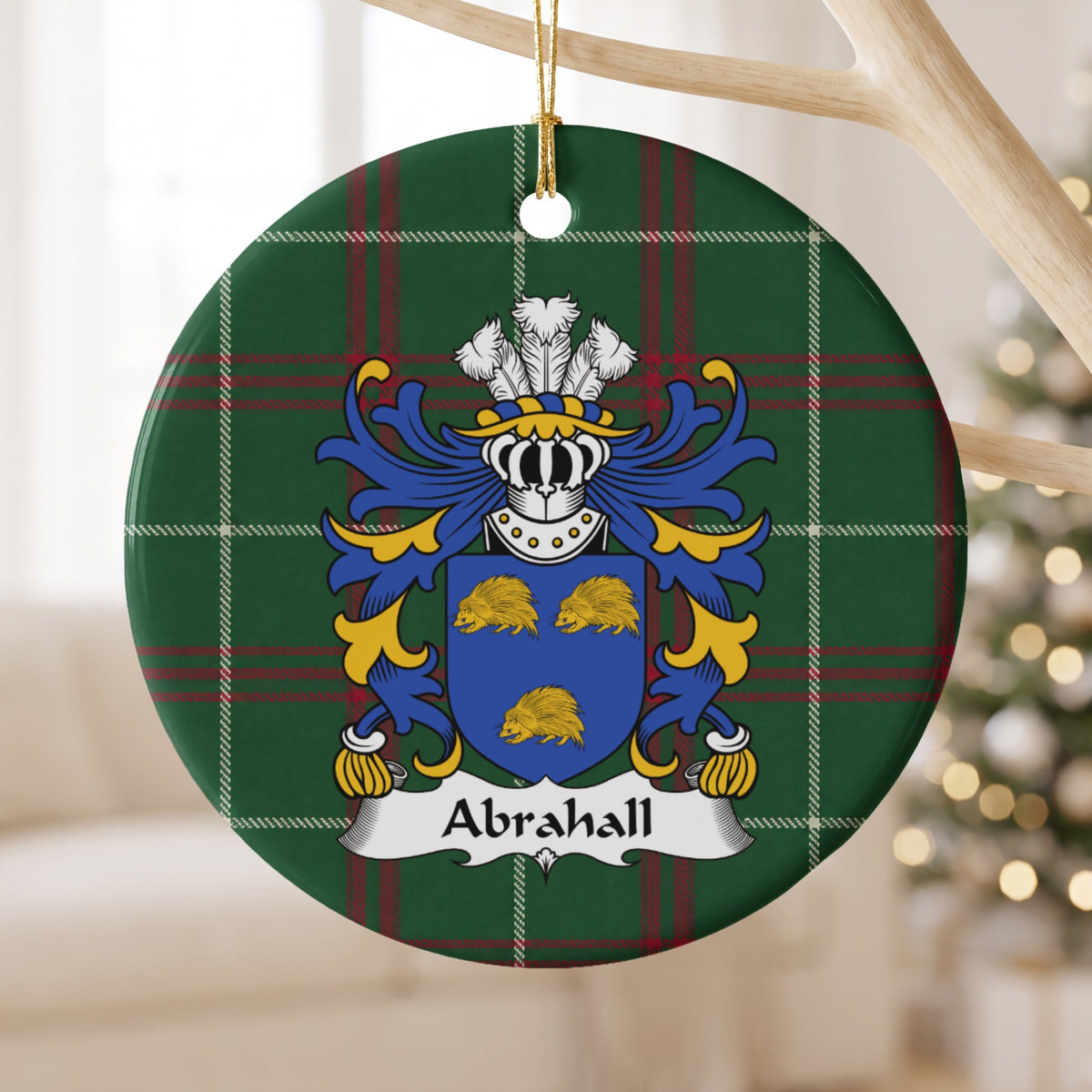 Abrahall family crest and surname on a round Welsh national tartan ornament, hanging by a gold cord from a pale wooden branch with blurred Christmas lights behind it.
