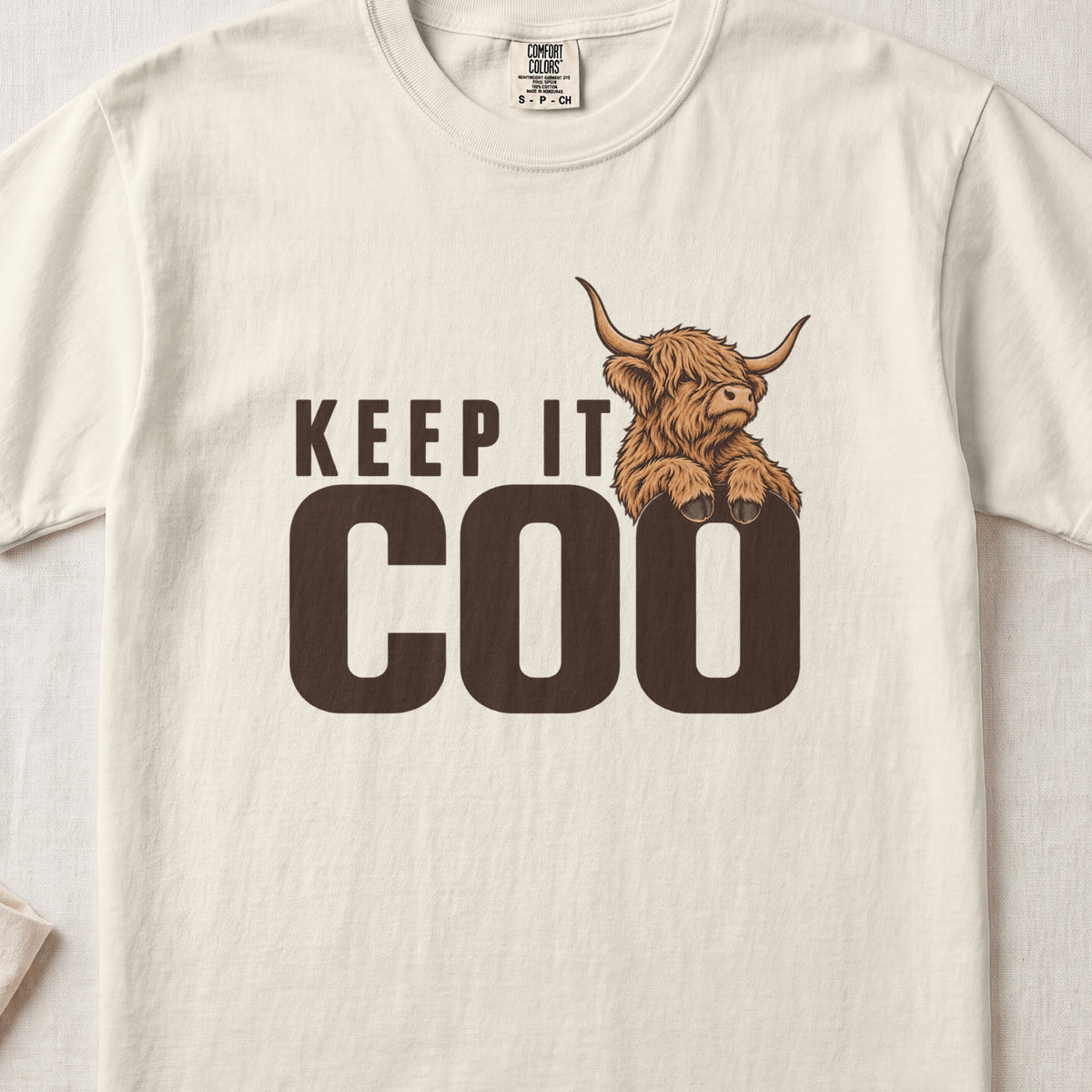 Keep It Coo Highland cow design on an Ivory Comfort Colors 1717 T-shirt, flat lay