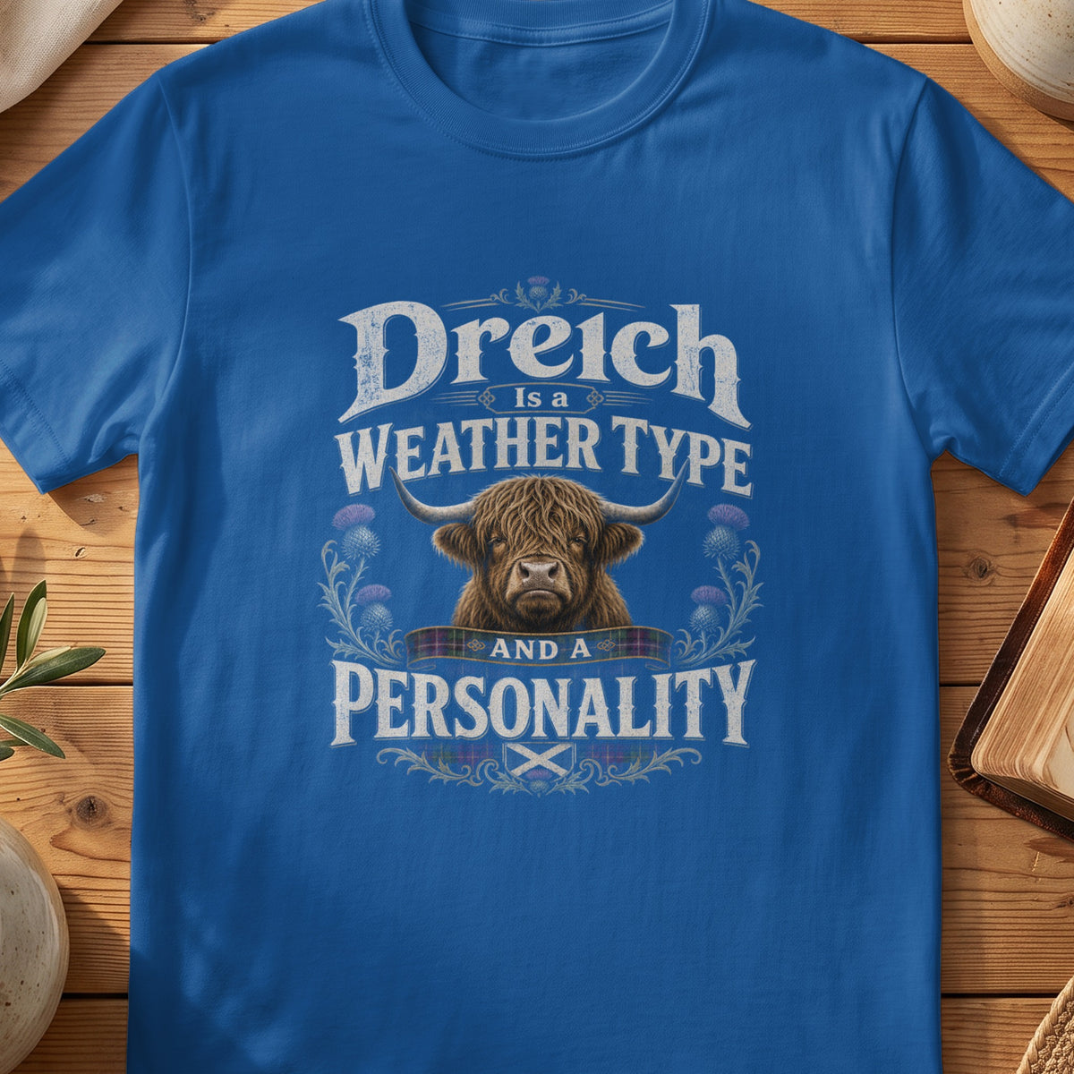 Blue t-shirt with highland cow graphic and text "Dreich Is a Weather Type And a Personality".