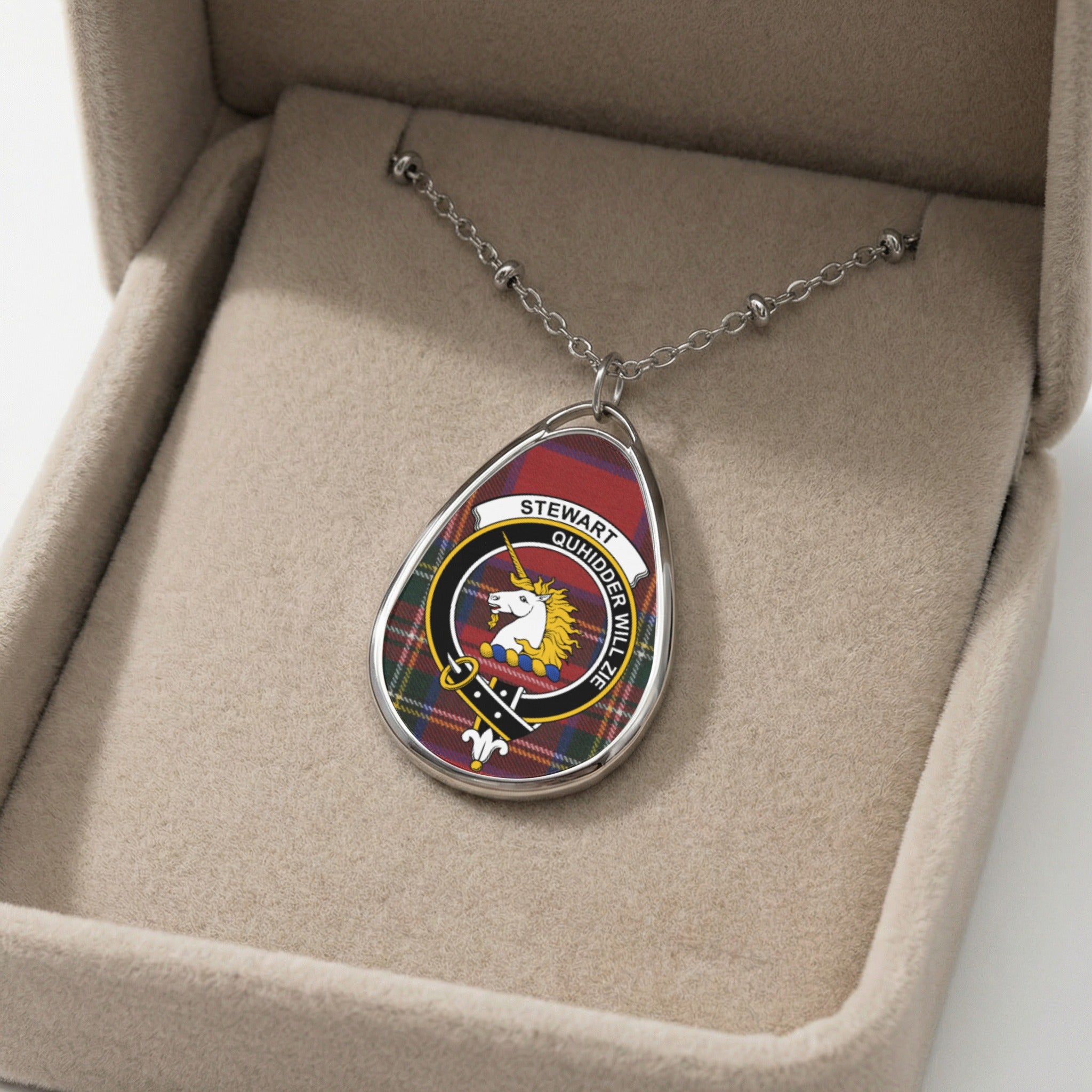 Oval pendant necklace with Stewart clan crest on tartan plaid background in a jewelry box.