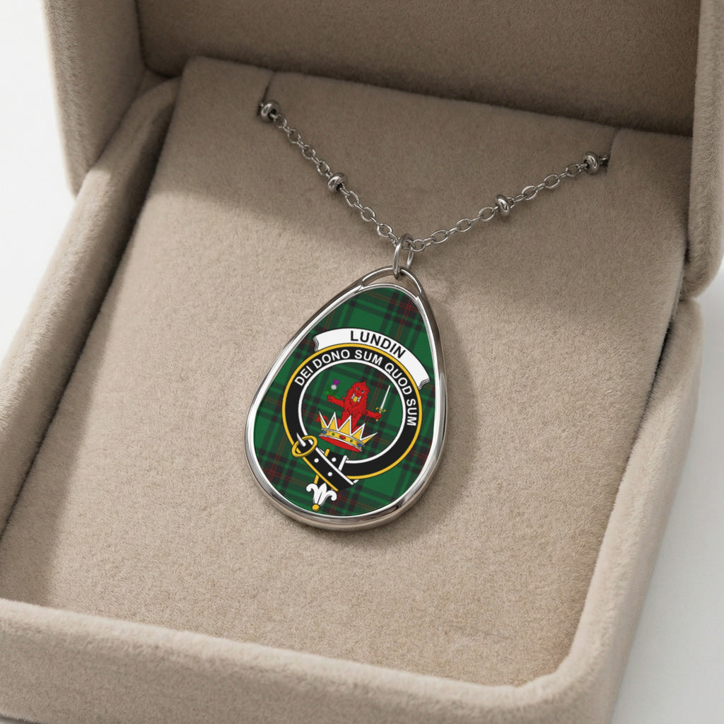 Oval pendant with Lundin crest on tartan, displayed in a beige jewelry box.