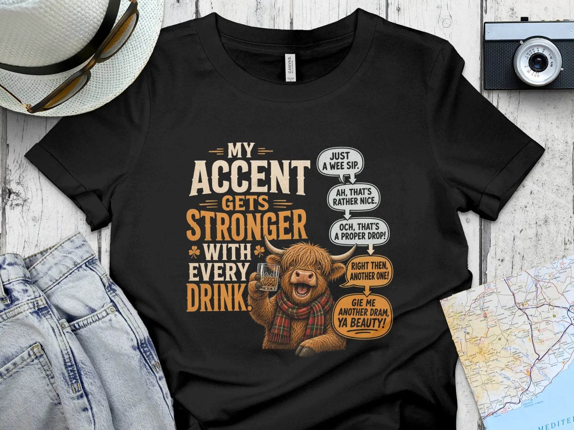 T-shirt with a Scottish Highland cow illustration and text about accents and drinks.
