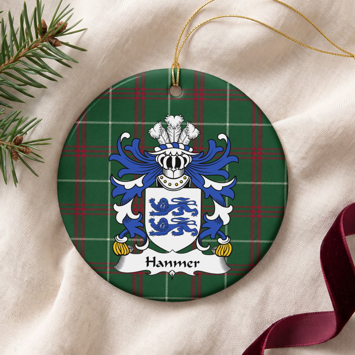 Hanmer ornament on cream fabric beside evergreen and burgundy ribbon, with gold string; two blue lions on a white shield.