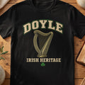 Doyle Irish harp T-shirt in Black, with cream surname lettering, a gold-toned harp, green shamrock and “Irish Heritage” text.