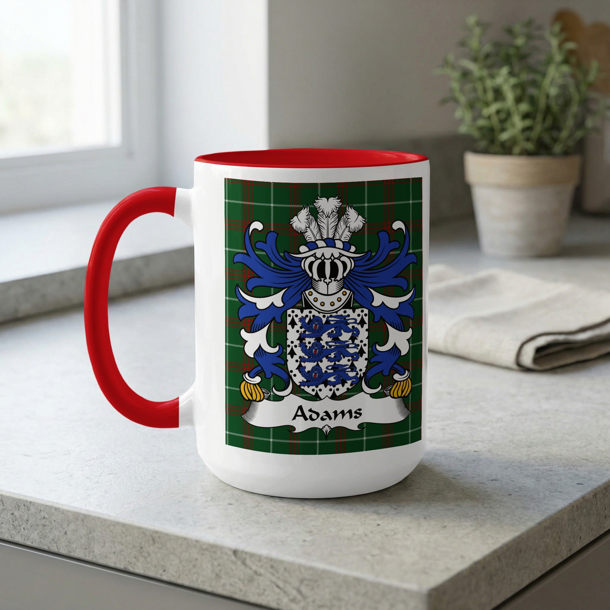 White mug with red handle displaying the Adams family crest on a green plaid background.