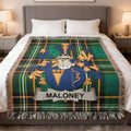 Maloney family crest on green plaid woven blanket on a bed.