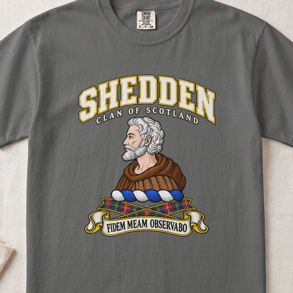 Shedden Scottish clan T-shirt in Pepper, front view with a gray-haired, bearded figure in a brown robe and motto design.