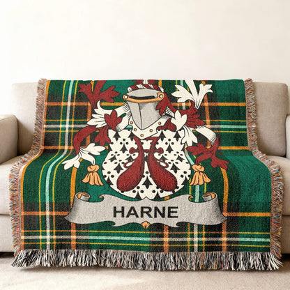 Green plaid throw blanket with HARNE crest and tasseled fringe on a sofa.