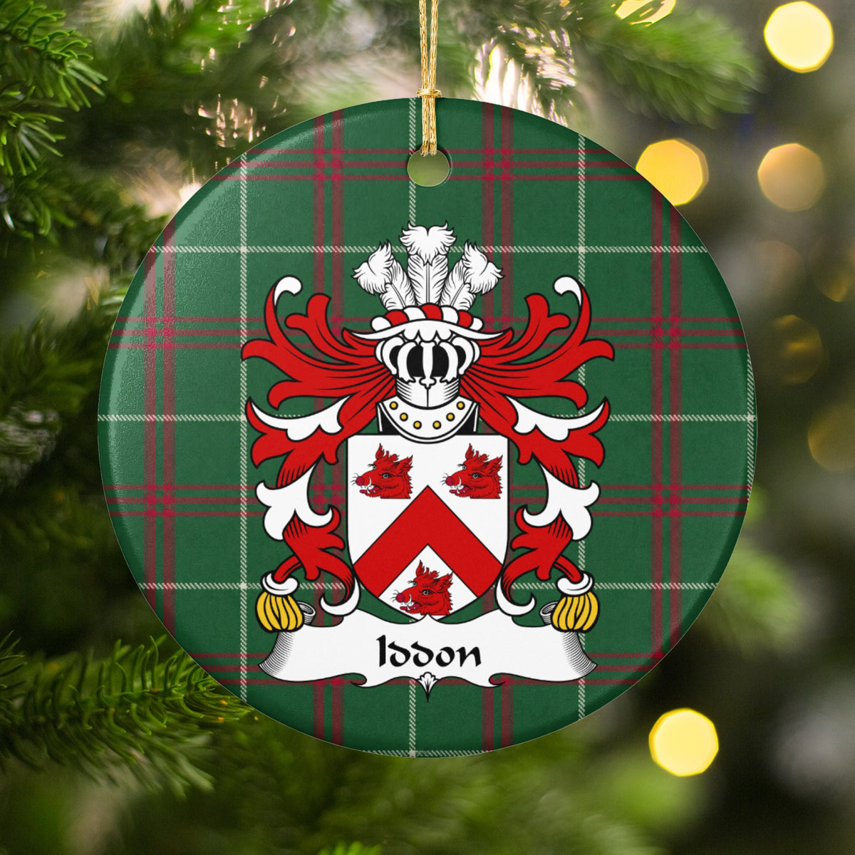 Iddon ornament hanging among Christmas tree branches and warm lights; a red chevron and three red boar heads on a white shield on Welsh national tartan.