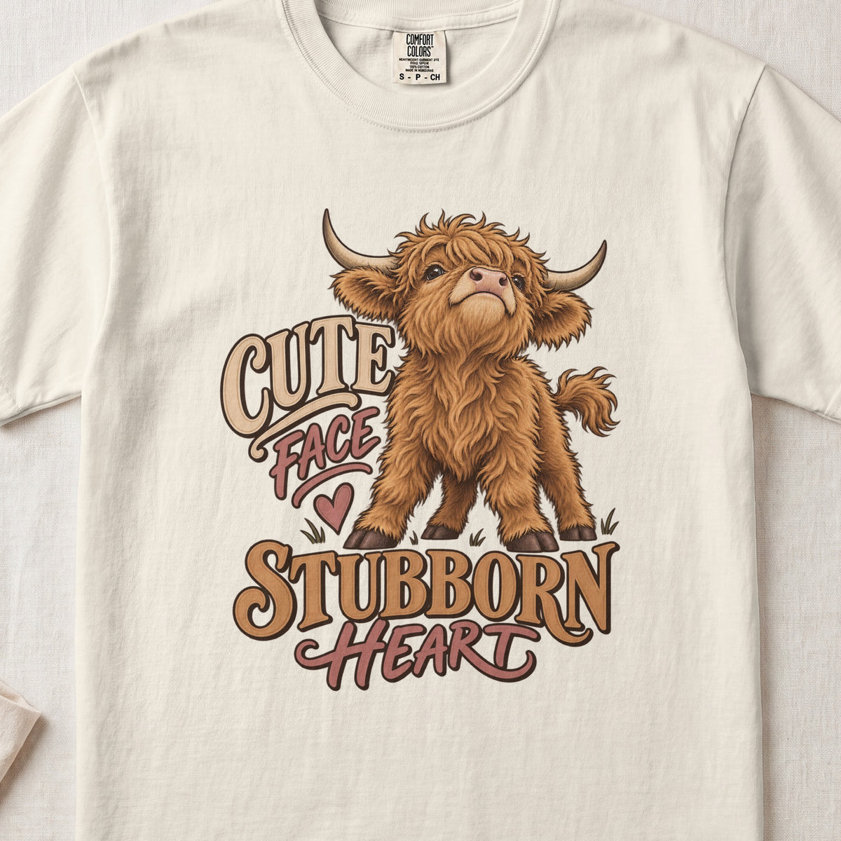 Cute Face, Stubborn Heart Highland cow design on an Ivory Comfort Colors 1717 T-shirt, flat lay