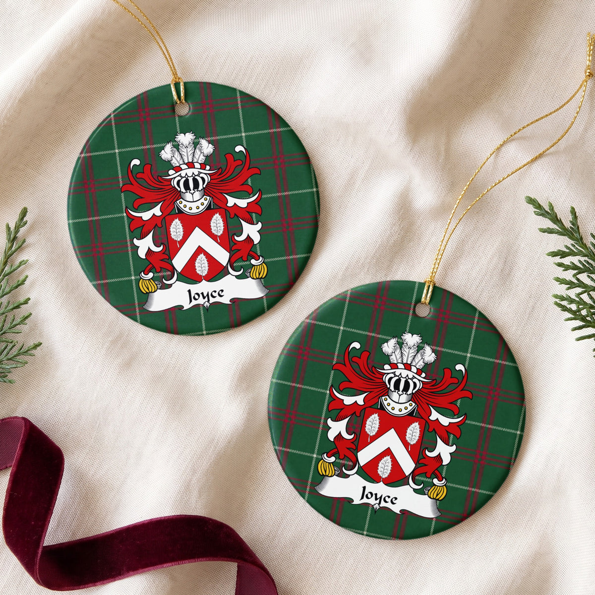 Two Joyce ornaments on cream fabric beside evergreen and burgundy ribbon; a white chevron and three white leaves on a red shield on Welsh national tartan.