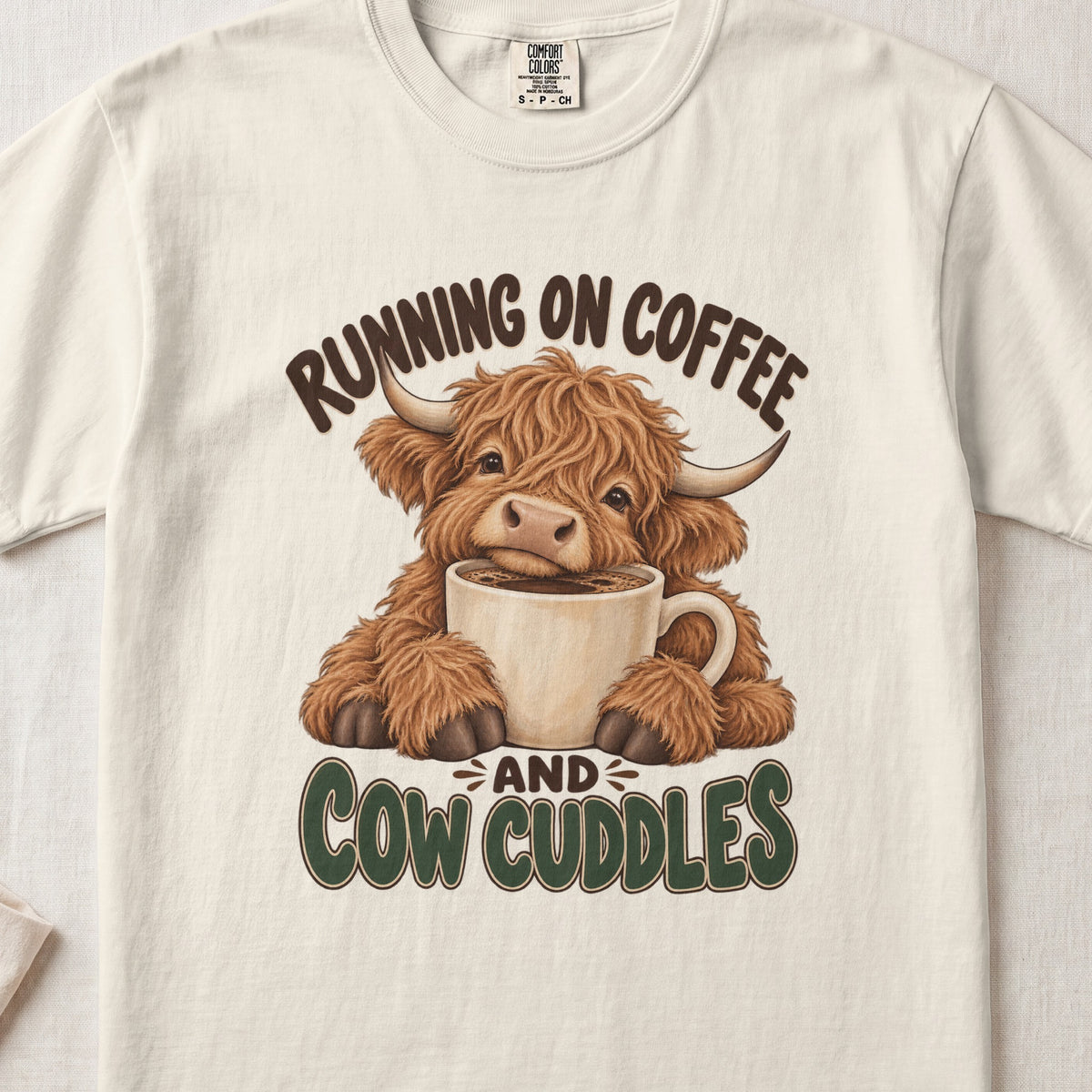 Running on Coffee & Cow Cuddles Highland cow design on an Ivory Comfort Colors 1717 T-shirt, flat lay