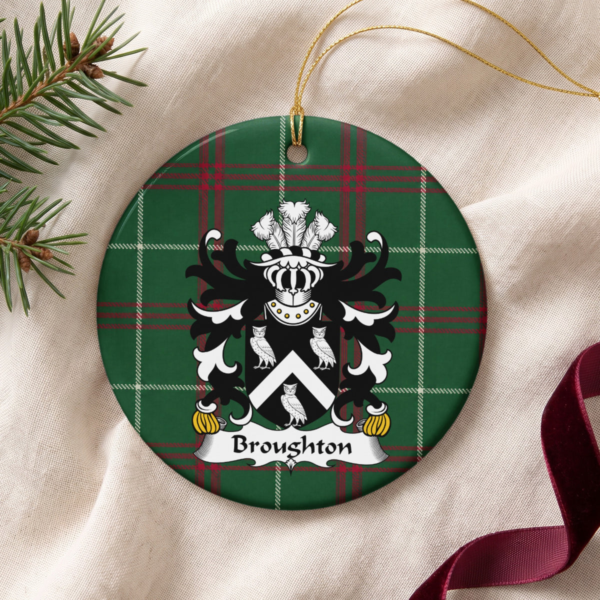 Broughton ornament on cream fabric with gold string, evergreen and burgundy ribbon; a white chevron between three white owls on black on Welsh national tartan.
