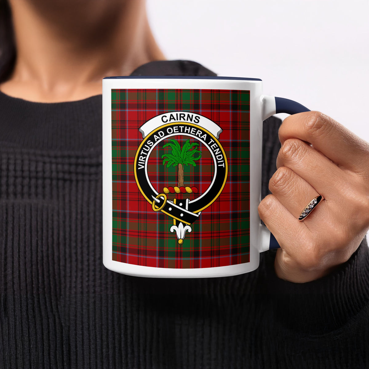 Close-up lifestyle view of Cairns Scottish family crest artwork on a navy 11 oz accent mug with a tartan background