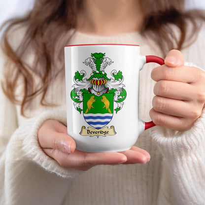 Mug with Beveridge family crest and red handle, held by person in white sweater.