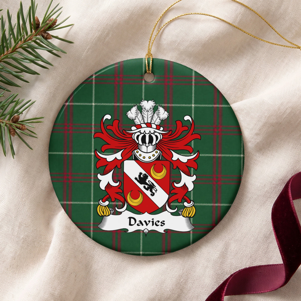 Davies Style 2 ornament on cream fabric with gold string, evergreen and burgundy ribbon; a black lion on a white diagonal band with two gold crescents on red.