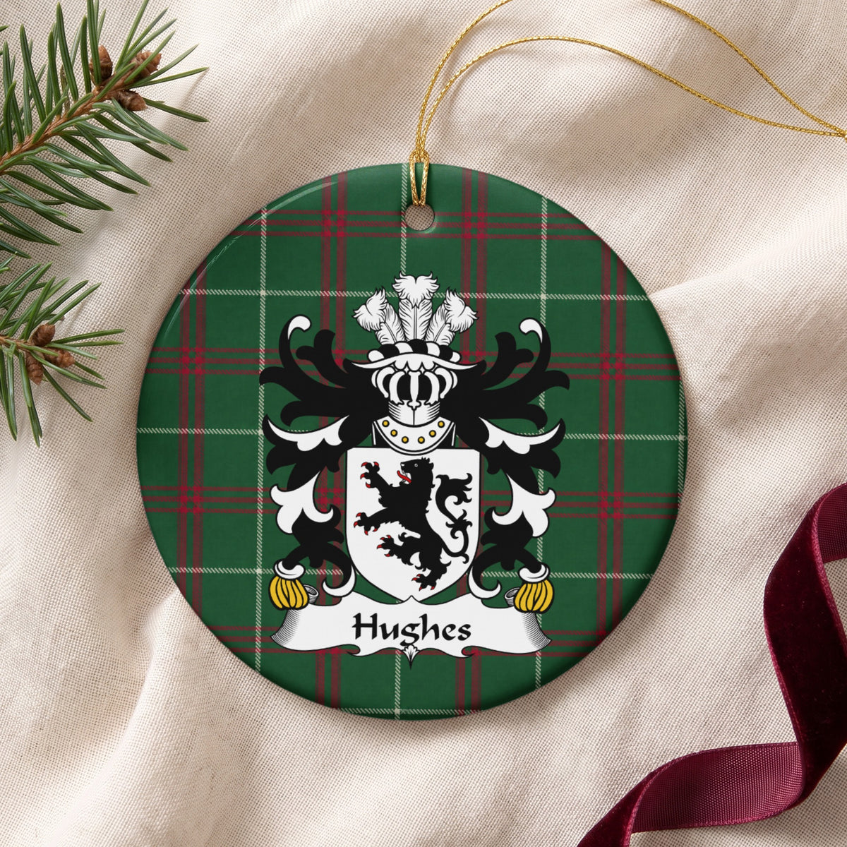 Hughes Style 2 ornament on cream fabric with gold string, evergreen and burgundy ribbon; a black lion on a white shield on Welsh national tartan.