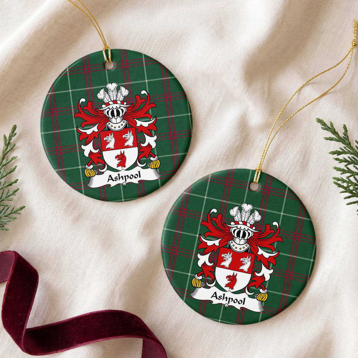 Two Ashpool ornaments on cream fabric with evergreen and burgundy ribbon; two white wolf heads above one red wolf head on a red-and-white shield on Welsh national tartan.