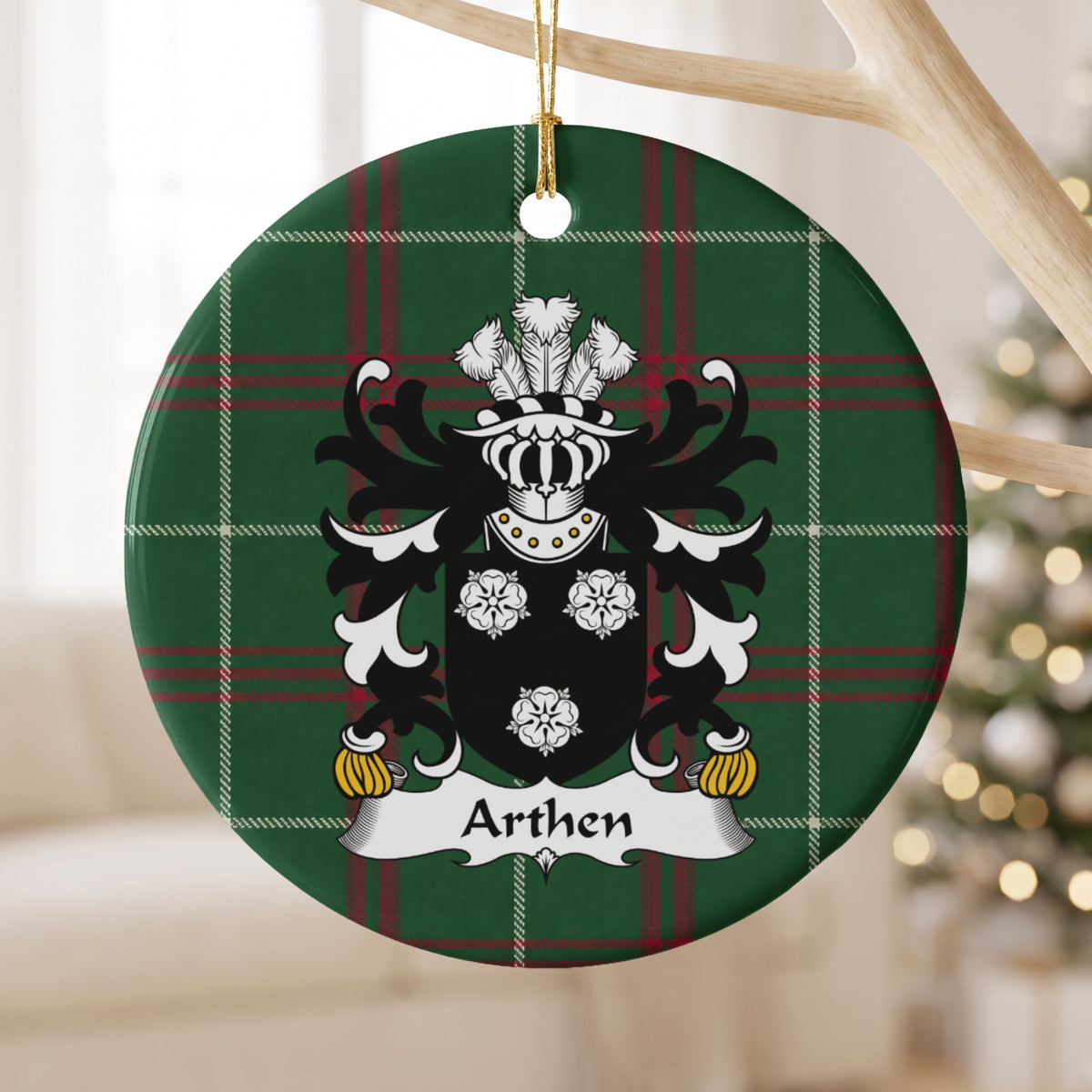 Arthen family crest and surname on a round Welsh national tartan ornament, hanging by a gold cord from a pale wooden branch with blurred Christmas lights behind it.