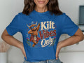 Blue t-shirt with a cartoon Highland cow wearing sunglasses and a kilt.