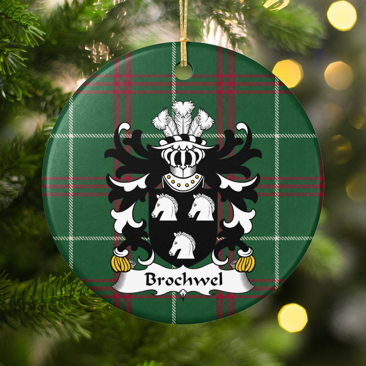 Brochwel Style 1 ornament hanging in a Christmas tree with warm lights; three white horse heads on a black shield on Welsh national tartan.