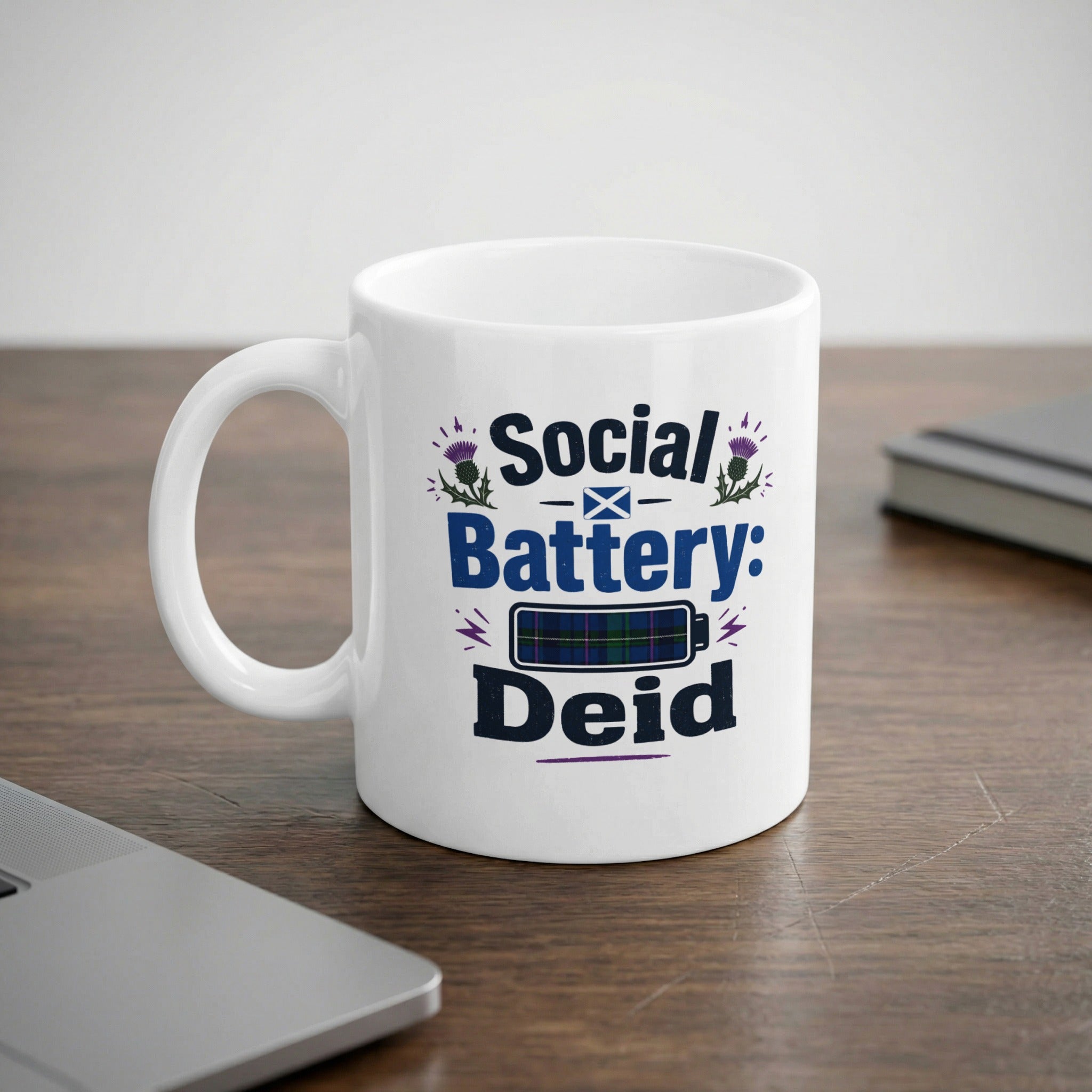 White mug with "Social Battery: Deid" text and Scottish tartan pattern.