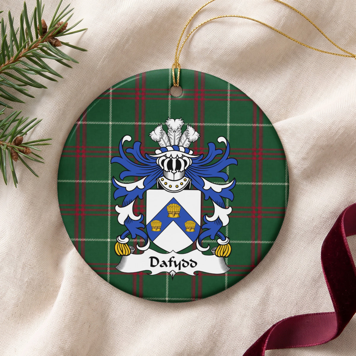 Dafydd Style 1 ornament on cream fabric with gold string, evergreen and burgundy ribbon; a blue chevron bearing three gold wheatsheaves on a white shield.