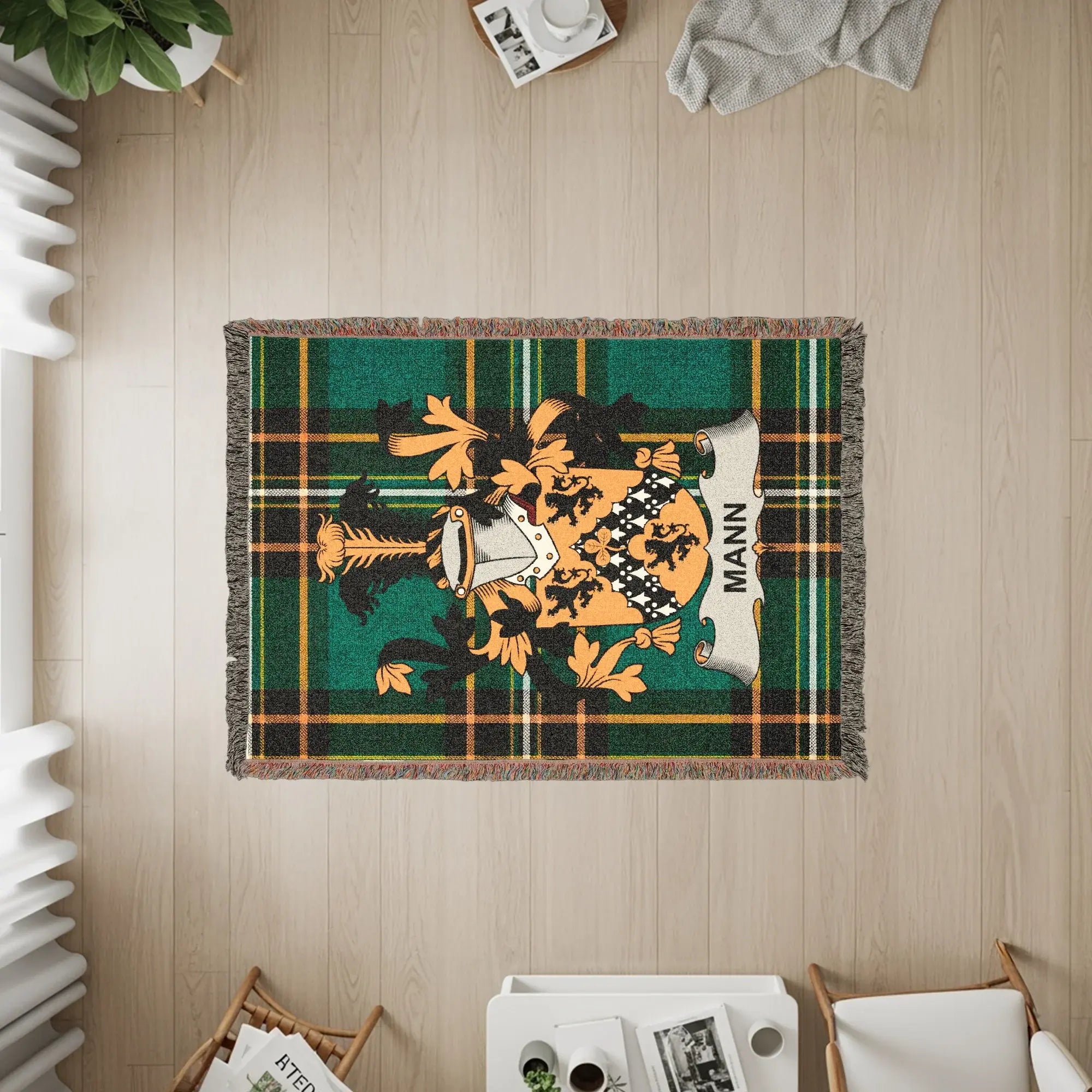 Tartan blanket with Mann family crest and fringe on a wooden floor.