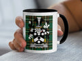White mug with black handle, featuring a family crest on plaid background.