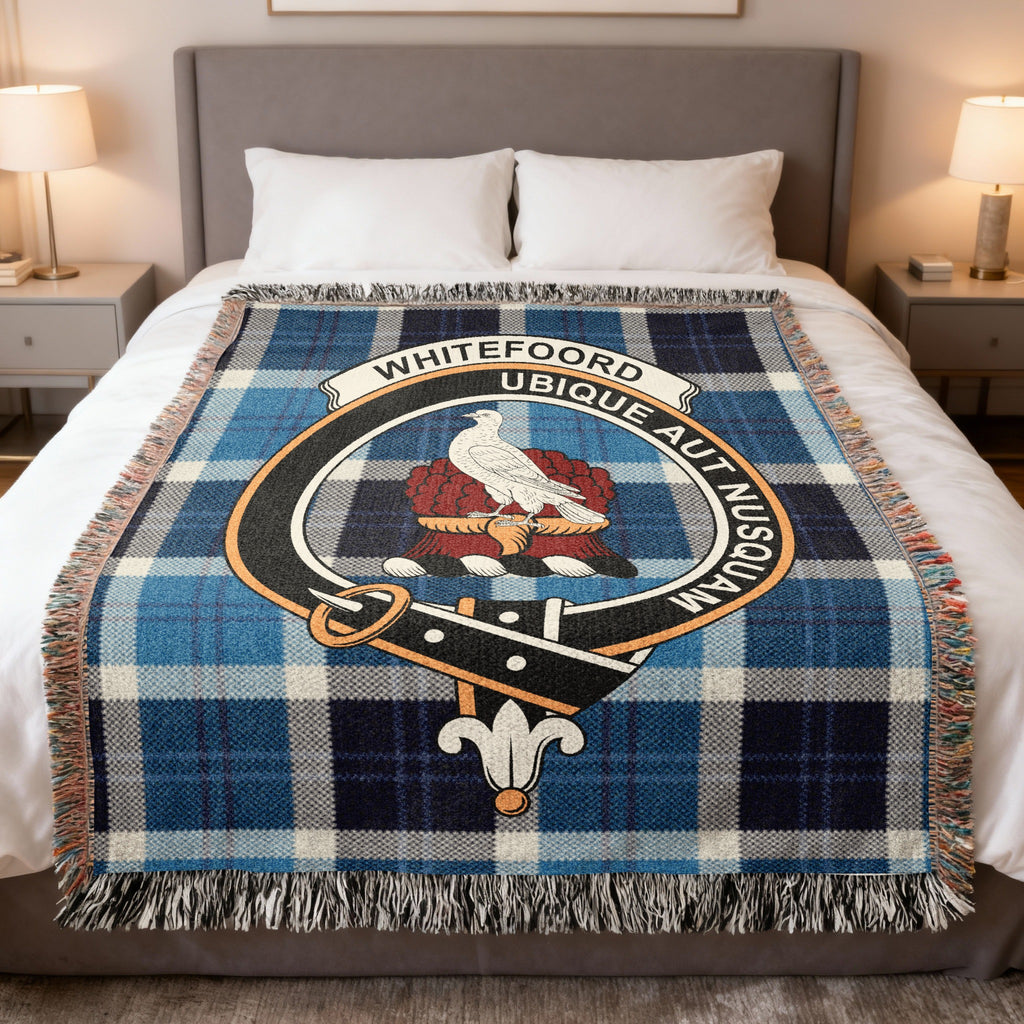 Whitefoord woven blanket displayed on a bed, with a white bird above a red crest base on a blue, black and white tartan background