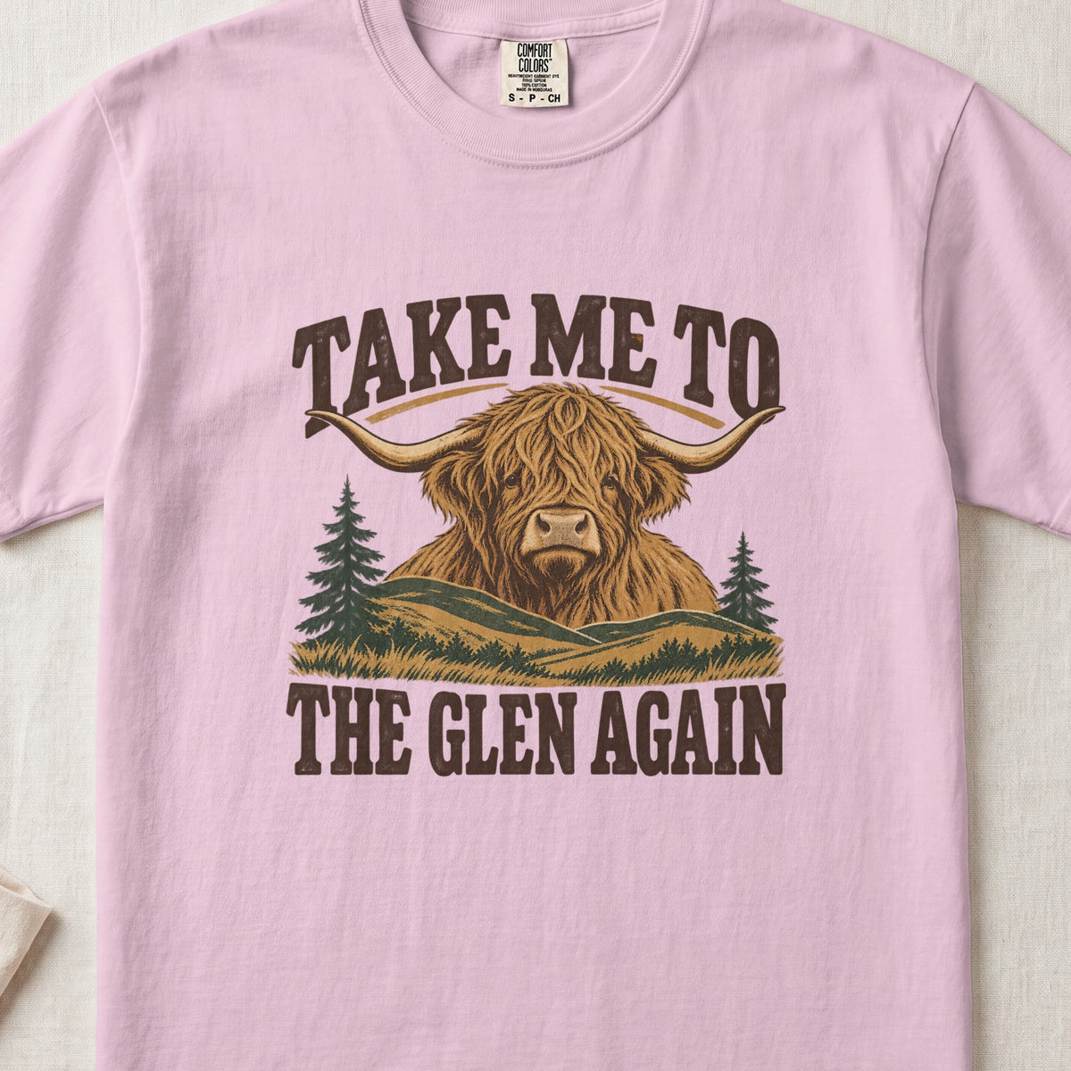 Take Me to the Glen Again Highland cow design on a Blossom Comfort Colors 1717 T-shirt, flat lay