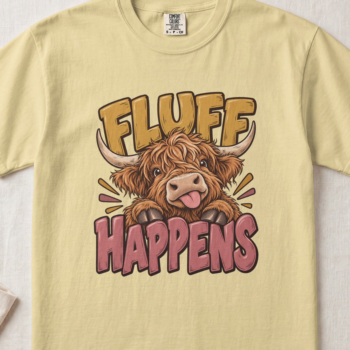 Fluff Happens Highland cow design on a Butter Comfort Colors 1717 T-shirt, flat lay