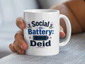 White mug with "Social Battery: Deid" text and tartan battery icon.