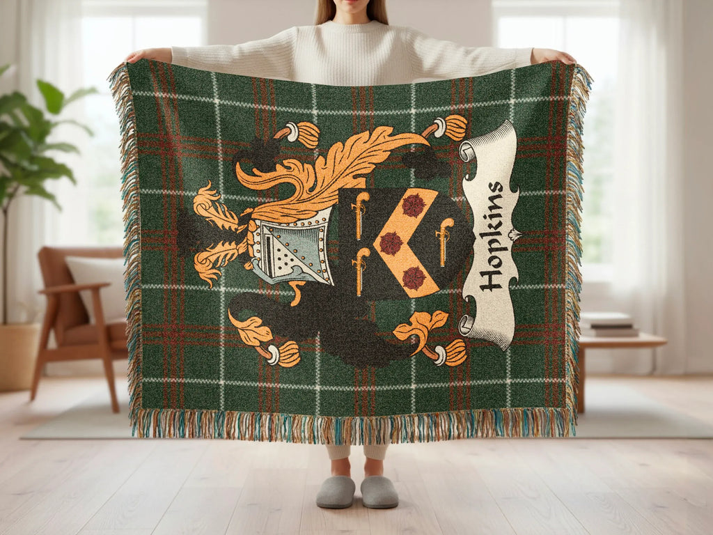 Green tartan blanket with Hopkins crest and fringe, held by person.