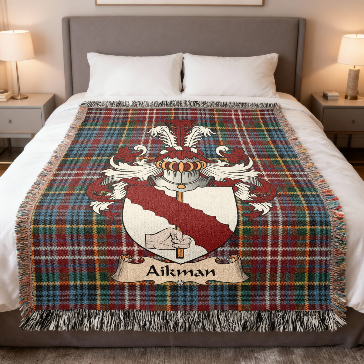Aikman Scottish family crest woven blanket on a Caledonia tartan background, displayed on a bed
