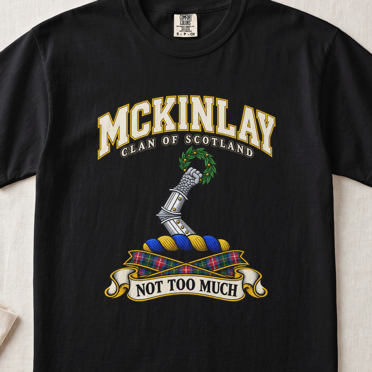 McKinlay Scottish clan T-shirt in Black, front view with an armored arm holding a green leafy wreath and motto banner.