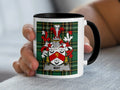 Mug with May family crest on green plaid background held in hand.