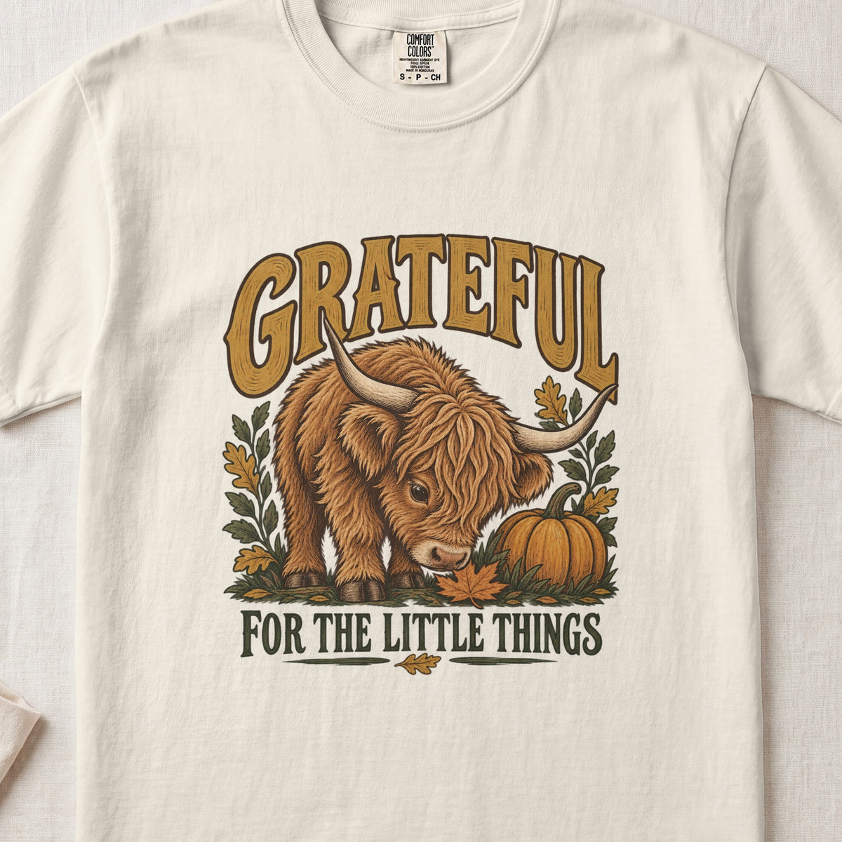 Grateful for the Little Things Highland cow design on an Ivory Comfort Colors 1717 T-shirt, flat lay