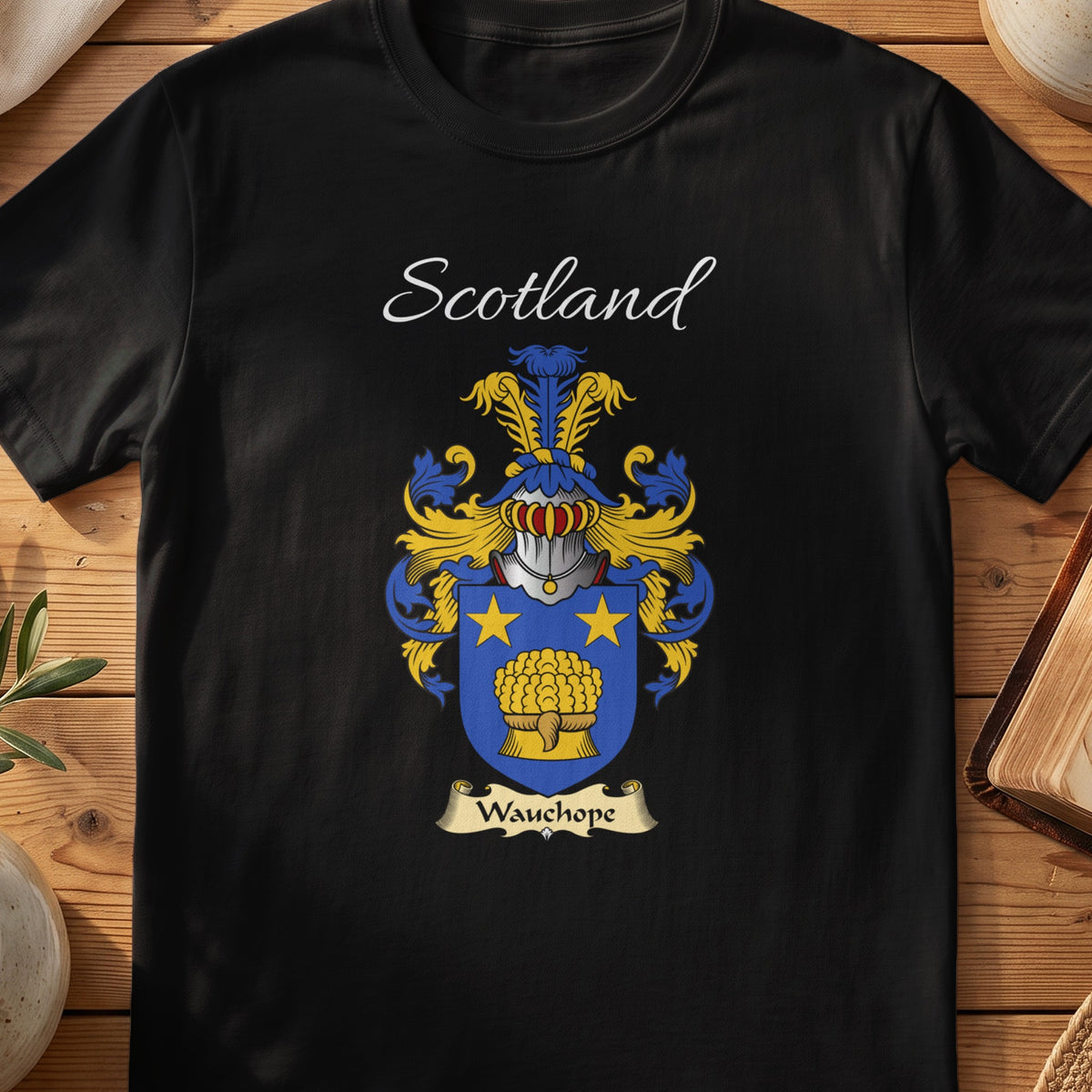 Black Wauchope Scottish family crest T-shirt laid flat, showing “Scotland” above a blue-and-gold shield with a barrel-like emblem and star.