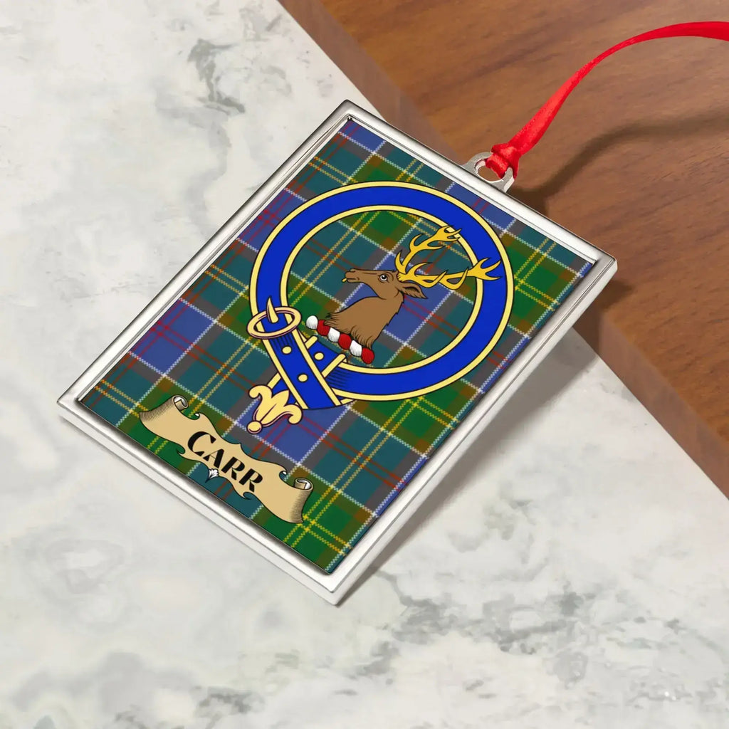 Carr ornament hanging from a Christmas tree branch by its satin ribbon