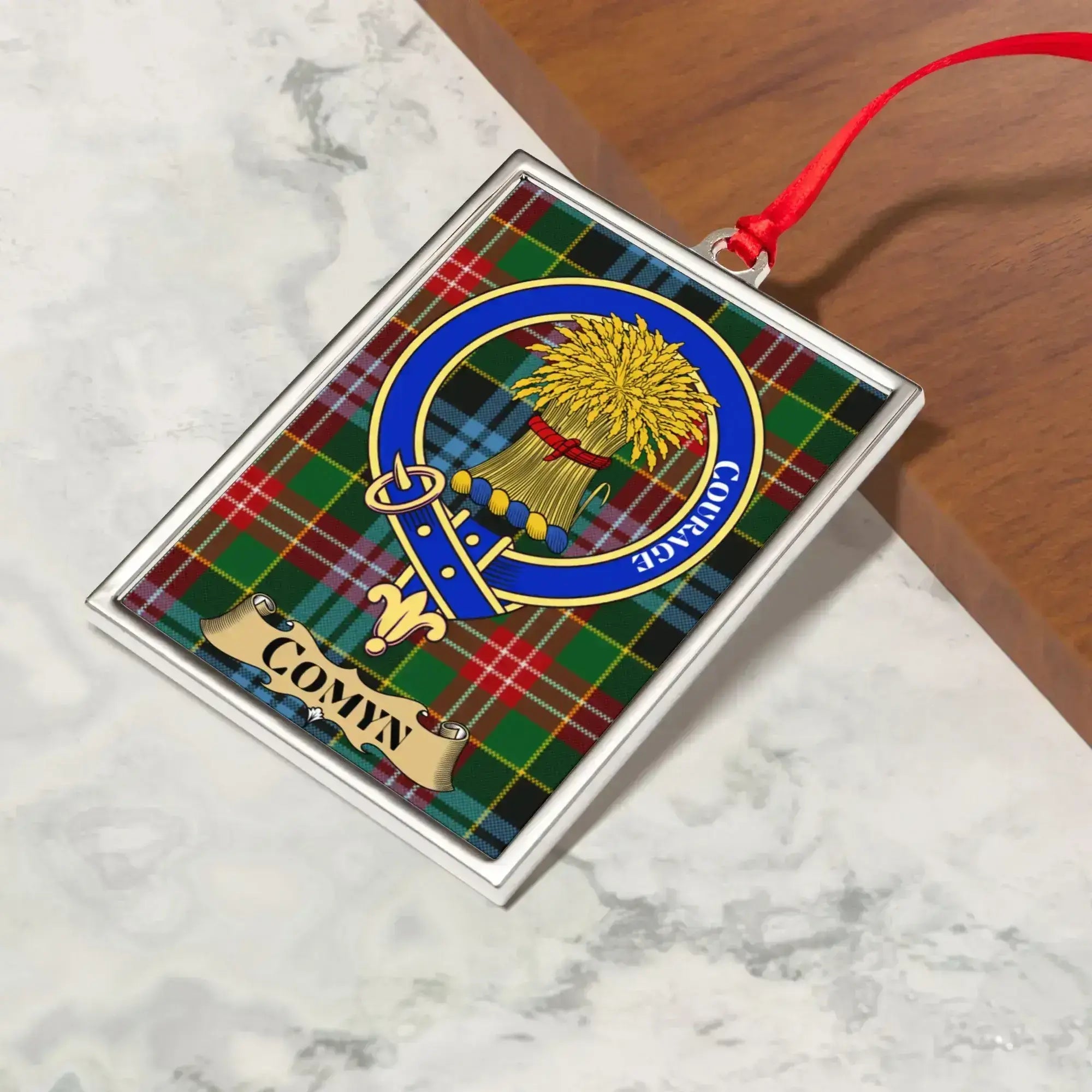 Comyn ornament hanging from a Christmas tree branch by its satin ribbon