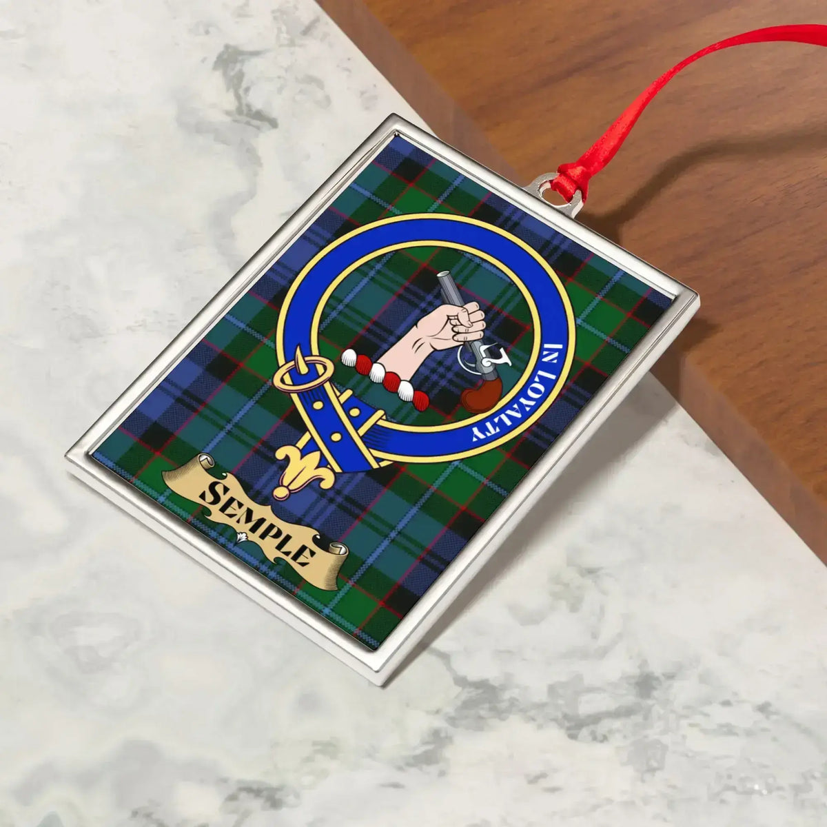Semple ornament hanging from a Christmas tree branch by its satin ribbon