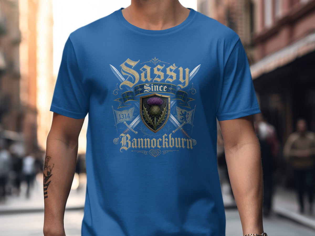 Blue t-shirt with a crest featuring a thistle, swords, and the text "Sassy Since Bannockburn 1314".